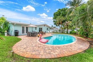 A backyard with a swimming pool, a flamingo float, and a patio area with outdoor furniture.