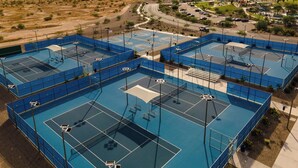 Vue aérienne d’un complexe sportif comprenant plusieurs courts de tennis, entouré d’un parking et d’un paysage pittoresque.