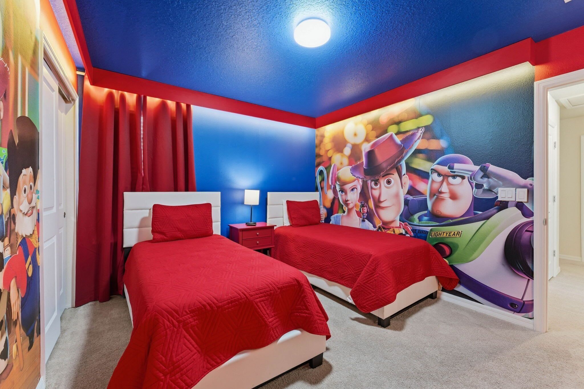A room with two beds, red bedding, a mural of Buzz Lightyear, and a red and blue color scheme.