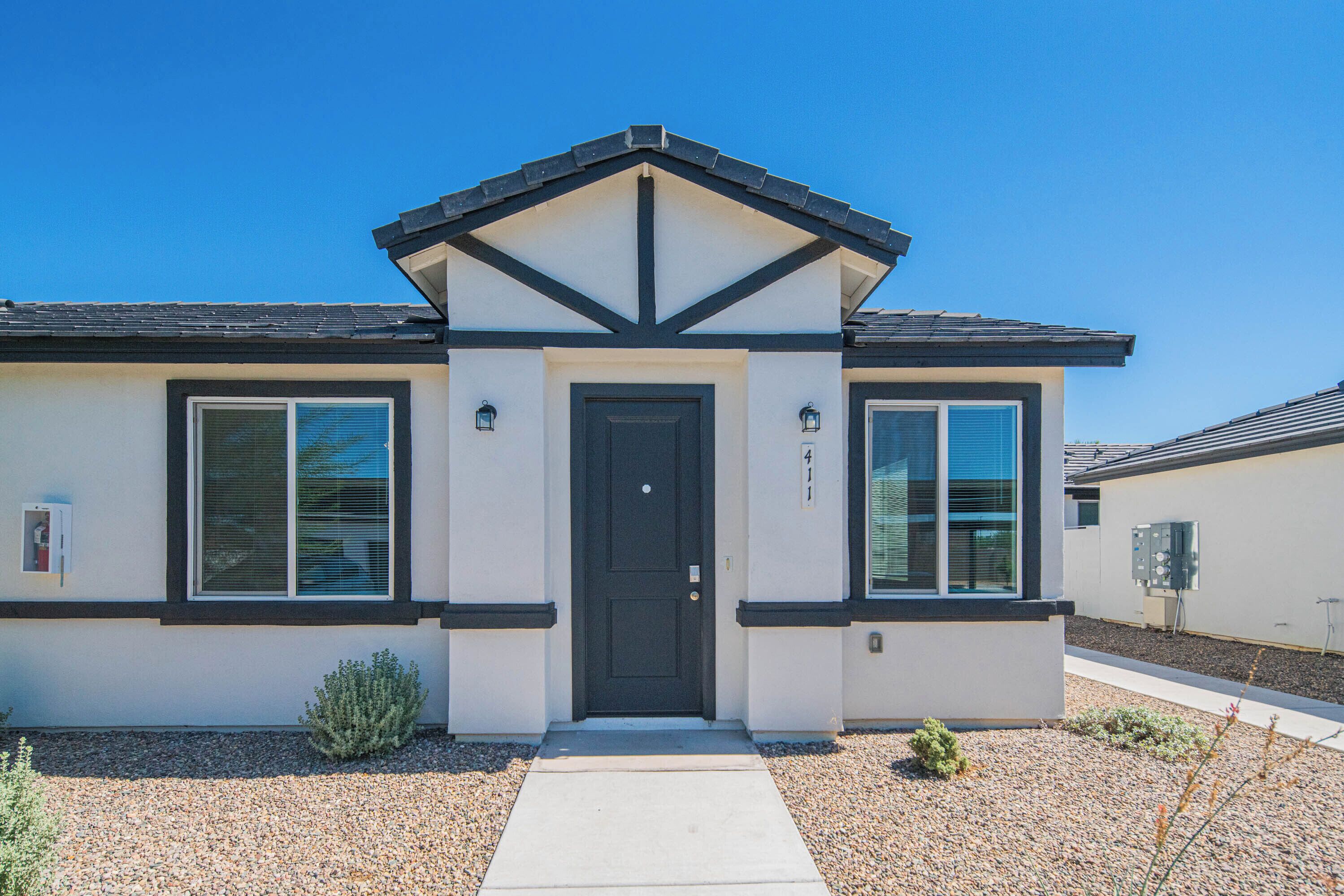 A modern two-story house with a black door, large windows, and a gravel driveway.