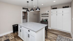 Una cocina con una isla central, luces colgantes, armarios blancos y un cartel que dice 'FARMHOUSE'.