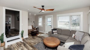 Una sala de estar moderna con sofá, reposapiés, ventilador de techo y una escalera que lleva a otra habitación.