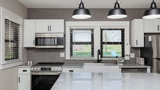 Una cocina moderna con armarios blancos, estufa de acero inoxidable, microondas y refrigerador.