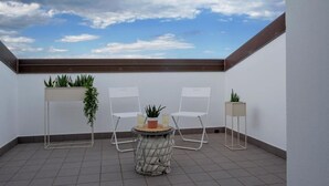 Eine Dachterrasse mit zwei weißen Stühlen, einem kleinen runden Tisch und Topfpflanzen.