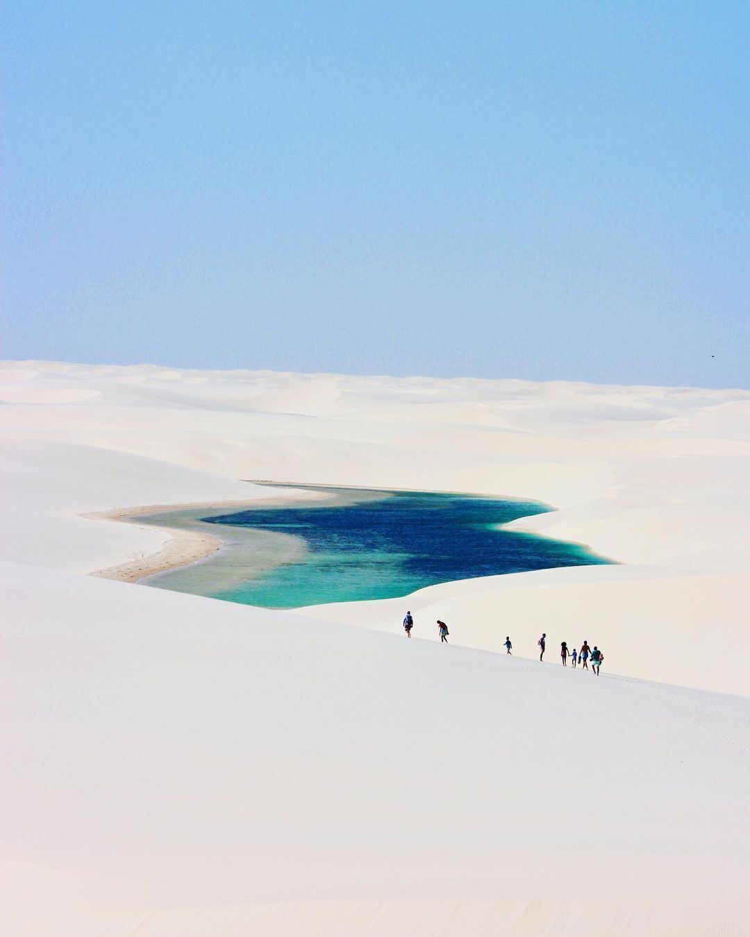 A vast white landscape with a group of people walking towards a blue water body.