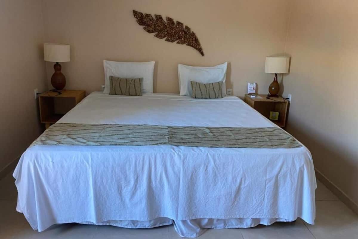 Un lit bien fait, recouvert d’une couvre-lit blanche et agrémenté de deux oreillers, avec deux tables de chevet de chaque côté, sur lesquelles sont posées des lampes.