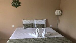 Camera d'albergo con un letto, due cuscini, un albero decorativo, un fiore e una lampada da comodino.