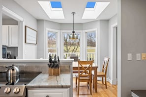 A kitchen with a central island, a dining area with two chairs, and a view through large windows. - Country Home with Hot Tub, Fire Pit, for 10 Guests! (Florence)