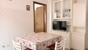 Un comedor con una mesa, sillas, un televisor y un mueble bar con puertas de cristal.