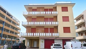 Un edificio de varios pisos con una puerta de garaje roja, un balcón en el segundo piso y un estacionamiento con varios vehículos.