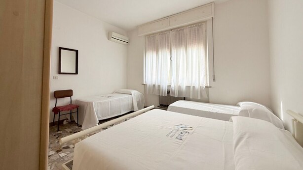 Habitación de hotel con dos camas, una silla, una mesita y una ventana con cortinas.