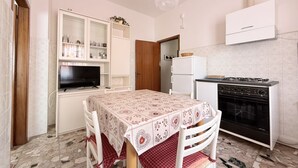 Una cocina con mesa, armarios, televisor y estufa.
