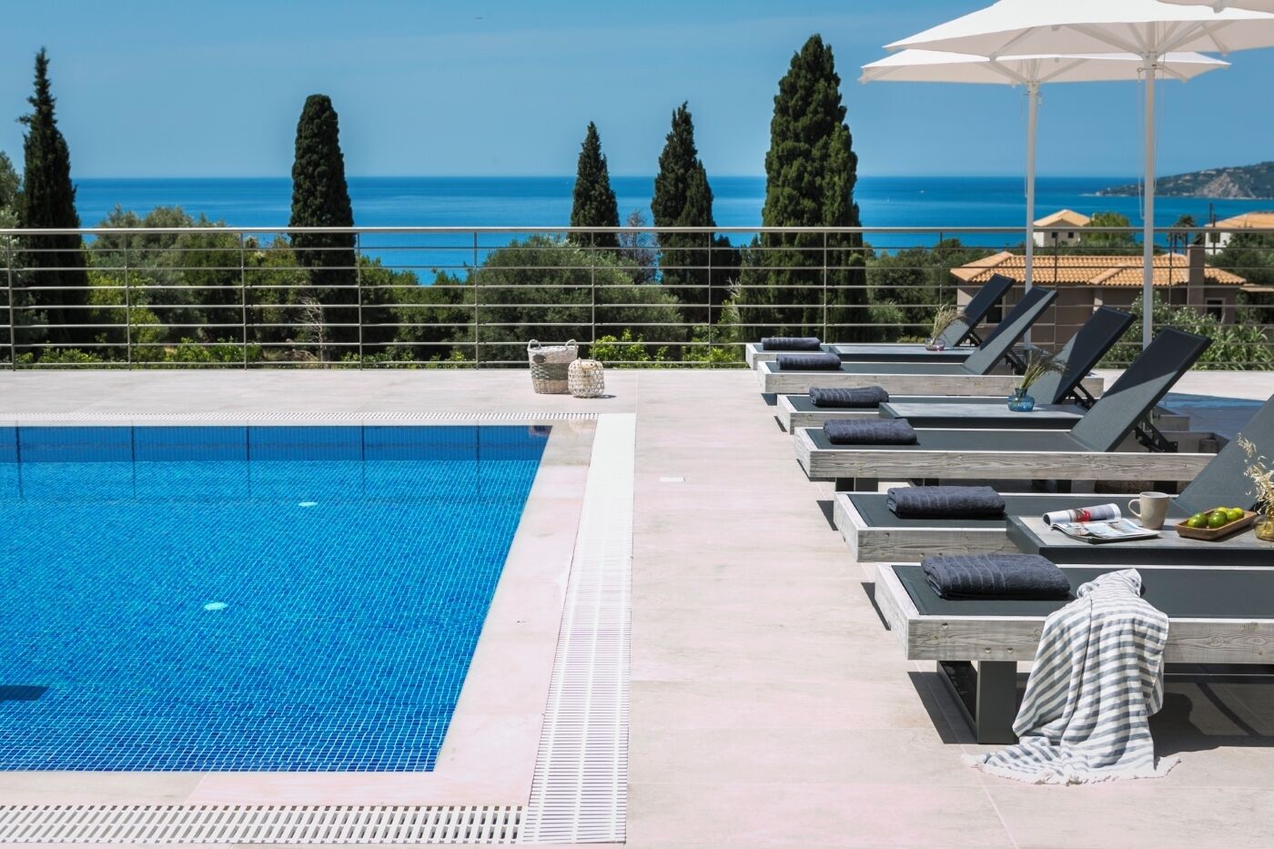 A pool area with lounge chairs and umbrellas, overlooking a clear blue sea.