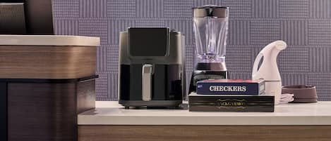 A kitchen area with a coffee maker, a blender, a kettle, and a book titled 'CHECKERS' on a countertop.