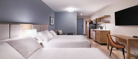 Habitación de hotel con dos camas, un escritorio, una silla, un televisor y una kitchenette.