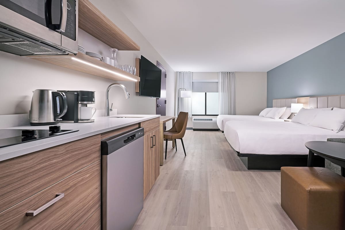 A modern hotel room with a kitchenette, a bed, a desk, and a seating area.