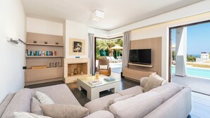 Een moderne woonkamer met een zithoek, een salontafel, een open haard, een televisie en uitzicht op een zwembad en groen.