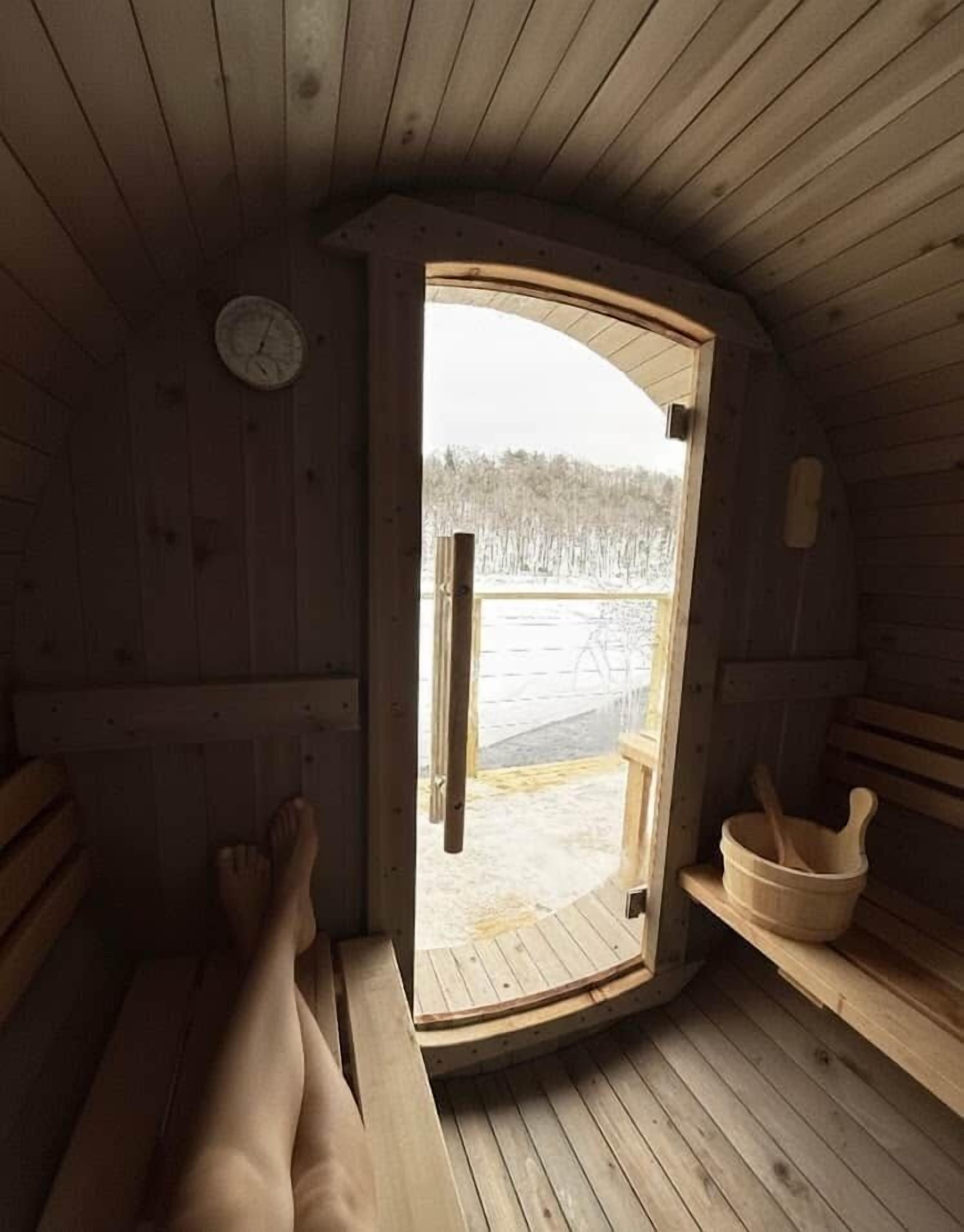 Ein Holzsaunaraum mit Bänken, einer Holztür, die nach draußen führt, und einem hölzernen Waschbecken.