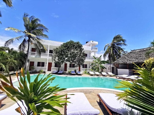 Un espace aménagé au bord de la piscine, avec des chaises longues, une piscine et un bâtiment doté de balcons.