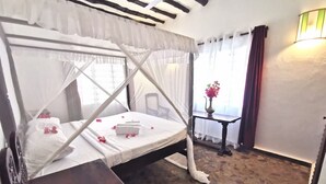 A room with a bed under a white canopy, a small table with a vase of flowers, and a stone floor. - Thami House Watamu (Watamu)