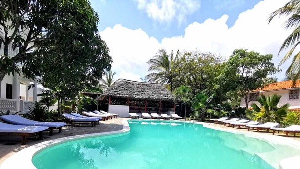 A swimming pool with lounge chairs around it, surrounded by trees and a building with a thatched roof. - Thami House Watamu (Watamu)