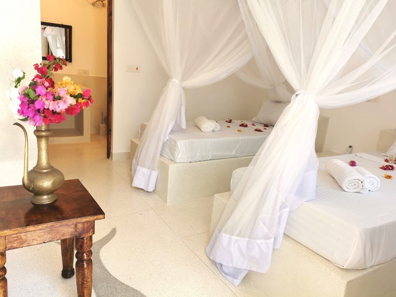 A hotel room with a bed under a canopy, a bedside table, and a vase with flowers.
