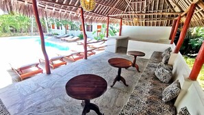 A covered outdoor seating area with a pool in the background. - Thami House Watamu (Watamu)