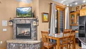 A cozy living room with a stone fireplace, a television mounted above it, and a dining area with wooden furniture. - Estes Park Retreat | 2 Kings | Near RMNP | ADA Friendly (Estes Park)