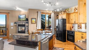 A modern kitchen with a stone fireplace, wooden cabinets, and a large island. - Estes Park Retreat | 2 Kings | Near RMNP | ADA Friendly (Estes Park)