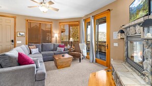 A living room with a sofa, armchair, coffee table, fireplace, and large windows with blinds. - Estes Park Retreat | 2 Kings | Near RMNP | ADA Friendly (Estes Park)