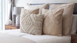 Un lit bien fait, avec une tête de lit, une table de chevet sur laquelle se trouve une lampe, et une œuvre d’art abstraite encadrée accrochée au mur.