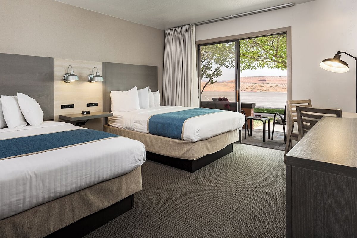 Quarto de hotel com duas camas, uma escrivaninha e uma cadeira. Há uma janela grande com vista para o deserto.