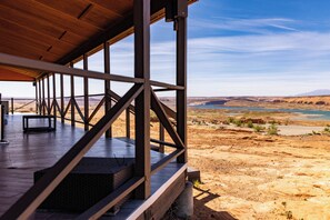 A covered outdoor area with a wooden deck, metal railings, and a view of a desert landscape with a body of water.