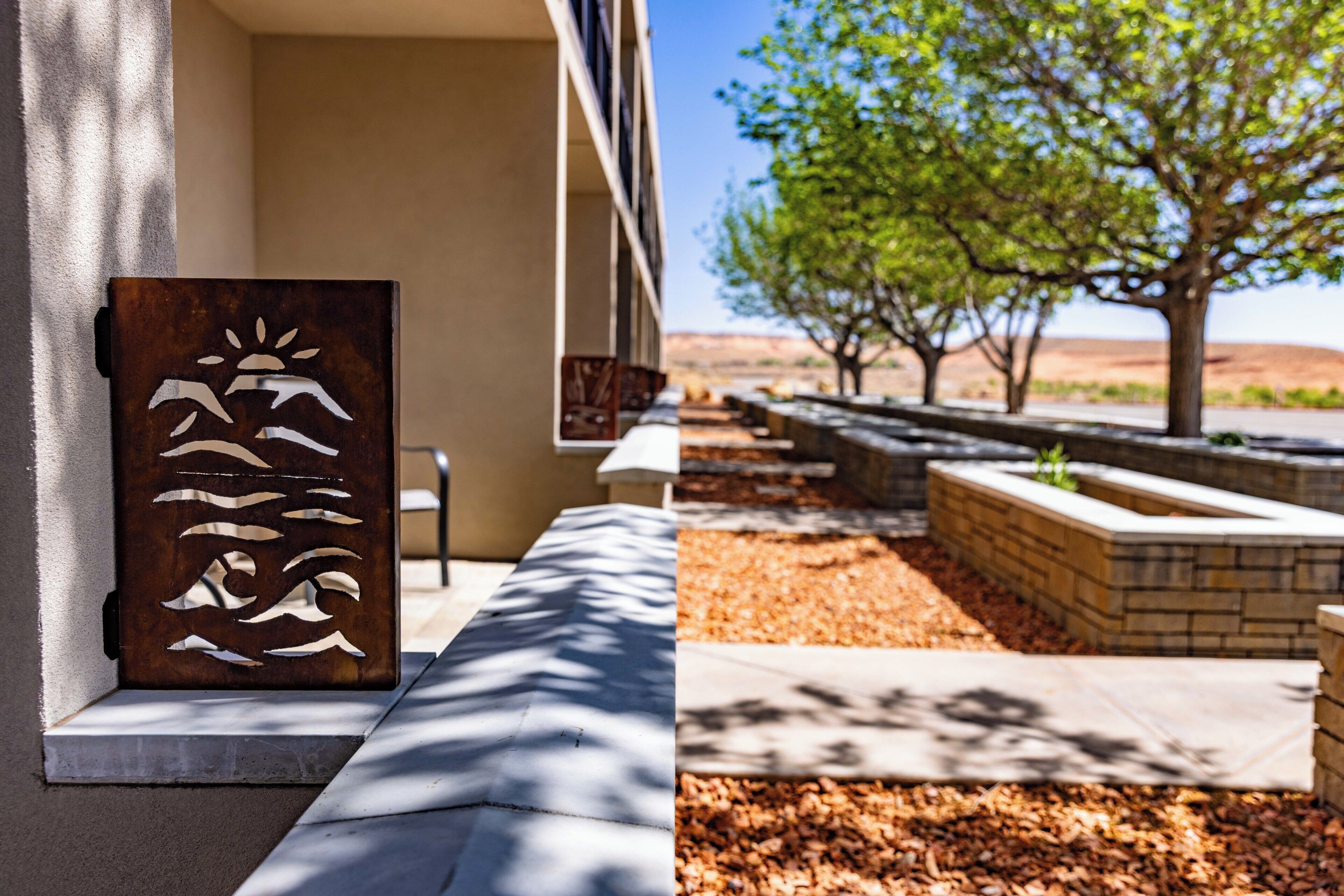 A metal sculpture with abstract figures, a pathway, and a landscaped area with trees and a view of distant hills.