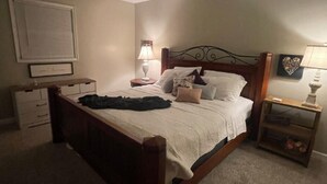 Een slaapkamer met een houten bed, een nachtkastje met een lamp, een dressoir en een ingelijst beeld aan de muur.