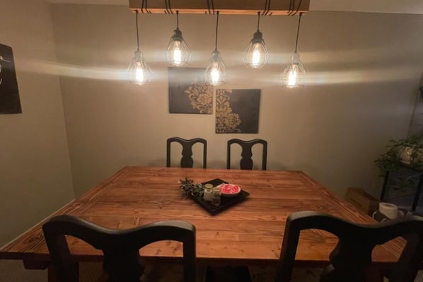 Ein Holzespeisetisch mit vier Stühlen, einer Ablage mit Obstschale und Gewürzen, sowie hängenden Lampen.