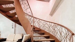 Un escalier en colimaçon dont la rampe est ornée de motifs représentant des branches d’arbre, menant à un palier agrémenté d’un canapé et d’une table basse.