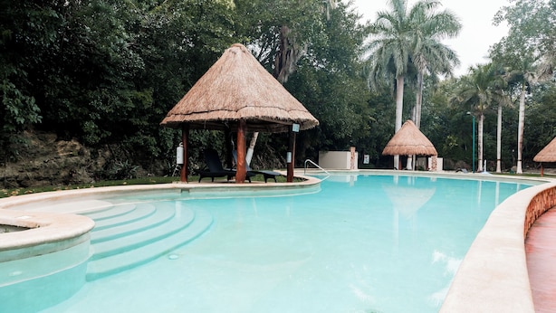 Une piscine bordée de structures à toits de chaume et de chaises longues.