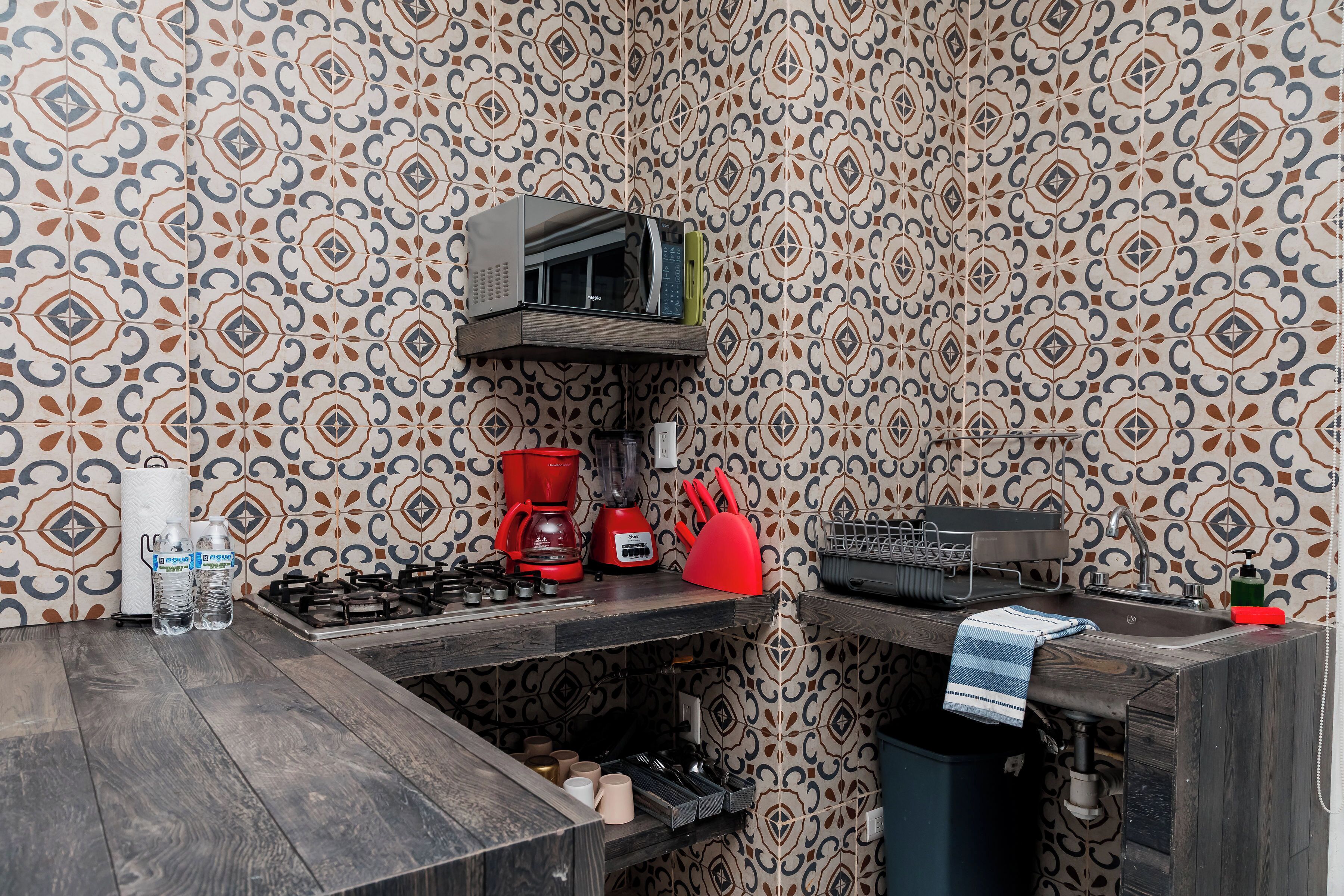 A kitchen with patterned wallpaper, a microwave, a coffee maker, and a sink.