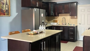 A kitchen with dark wooden cabinets, a central island, and a dining area with chairs. - Spacious 6-bedroom villa at Hellshire w/ private pool, games room & gym (Portmore)