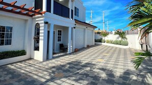 A two-story white house with a covered porch and a paved driveway. - Spacious 6-bedroom villa at Hellshire w/ private pool, games room & gym (Portmore)
