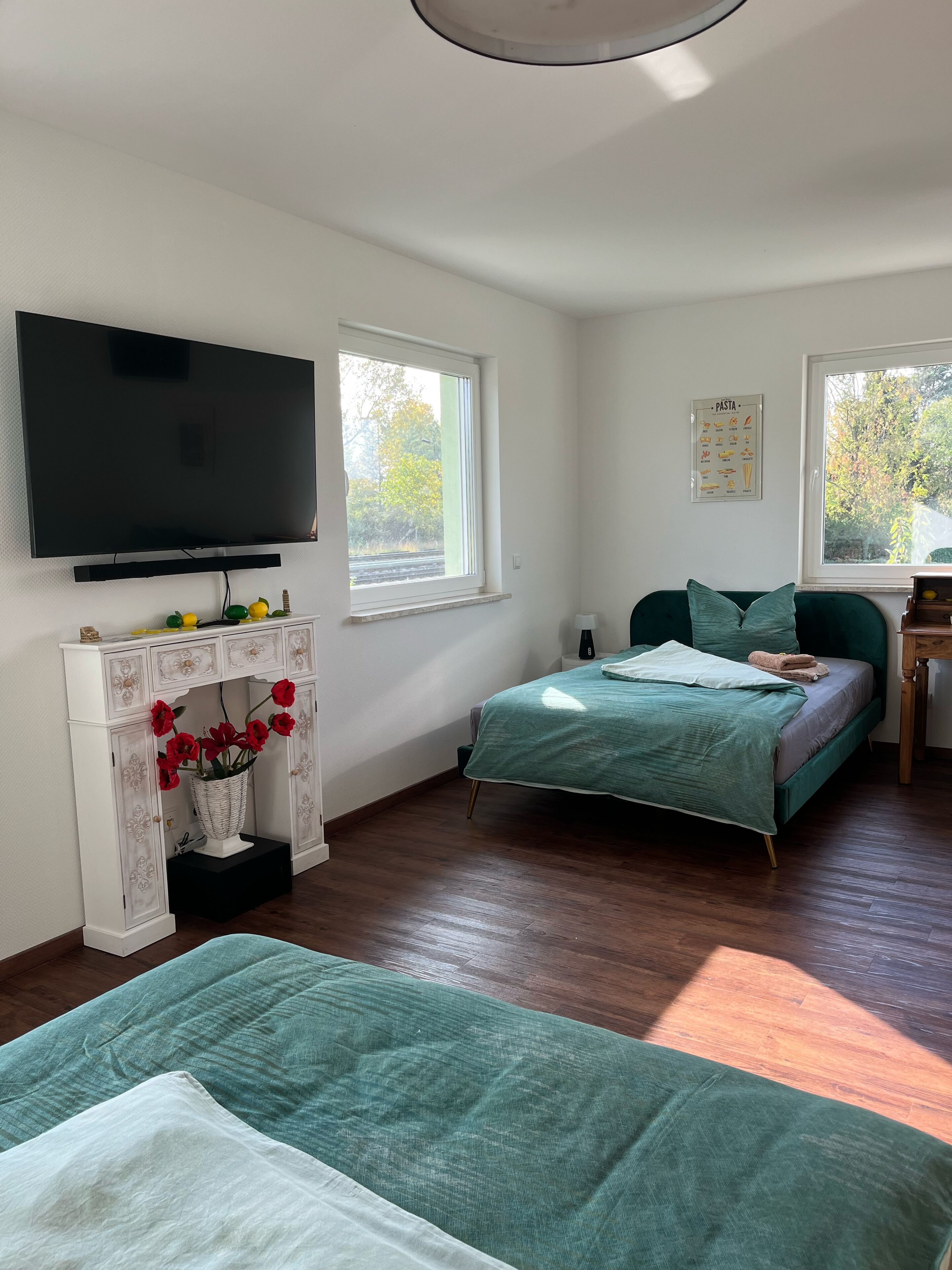 Quarto com cama, televisão na parede, janela e prateleira com objetos decorativos.