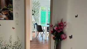 A room with a wooden floor, a door leading to a balcony, a wall clock, a framed picture, and a vase with flowers. - Ferienwohnungen im Grund 22 (Hoppegarten)
