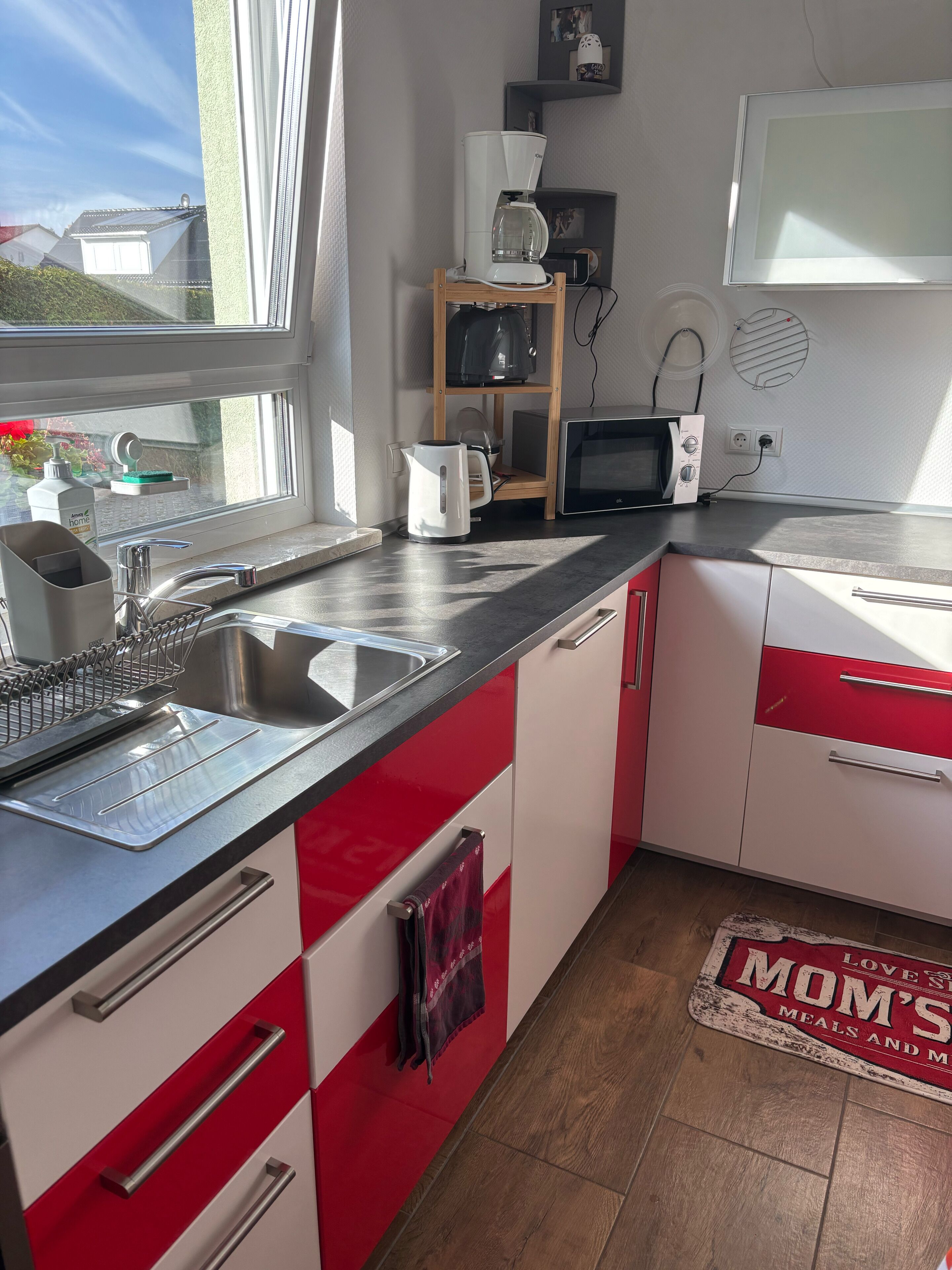 A kitchen with a sink, kettle, microwave, and a window.