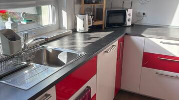 A kitchen with a sink, kettle, microwave, and a window.