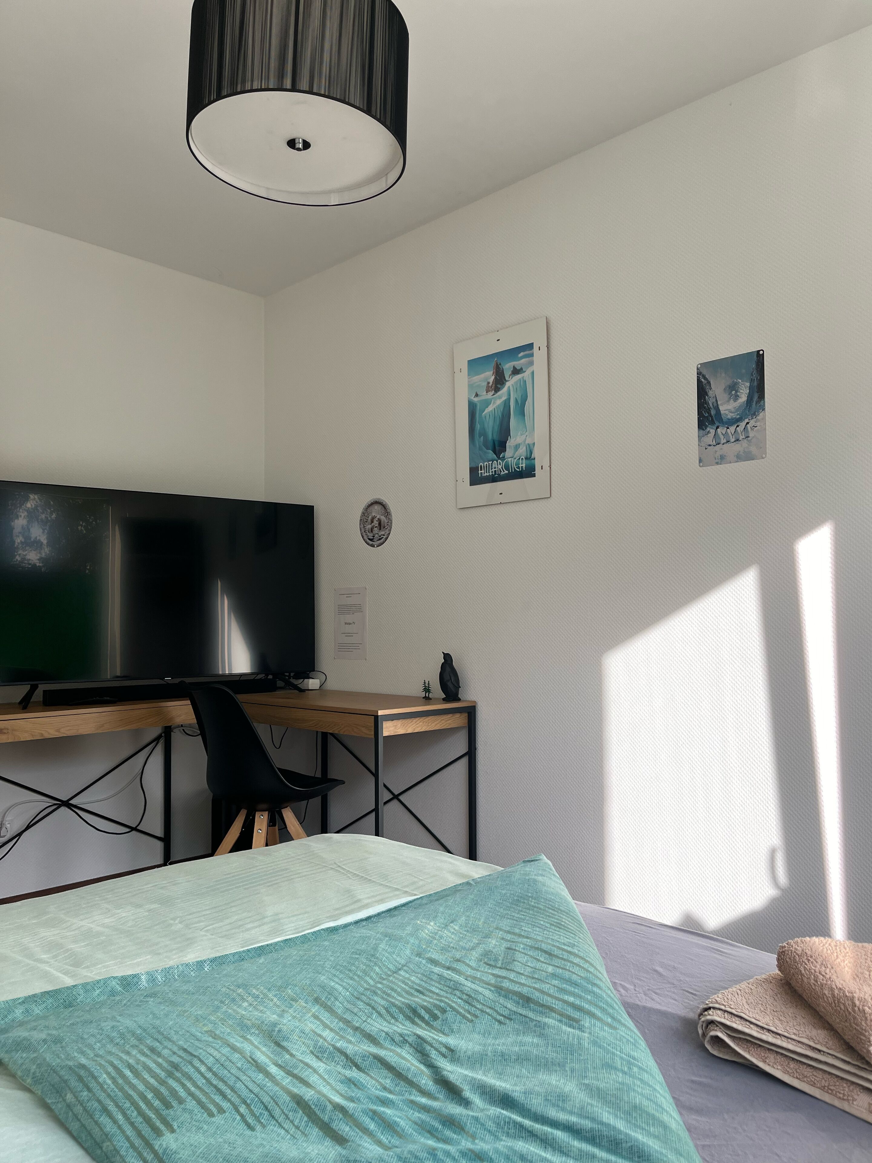 A bedroom with a bed, a desk with a computer, a television, and two framed pictures on the wall.