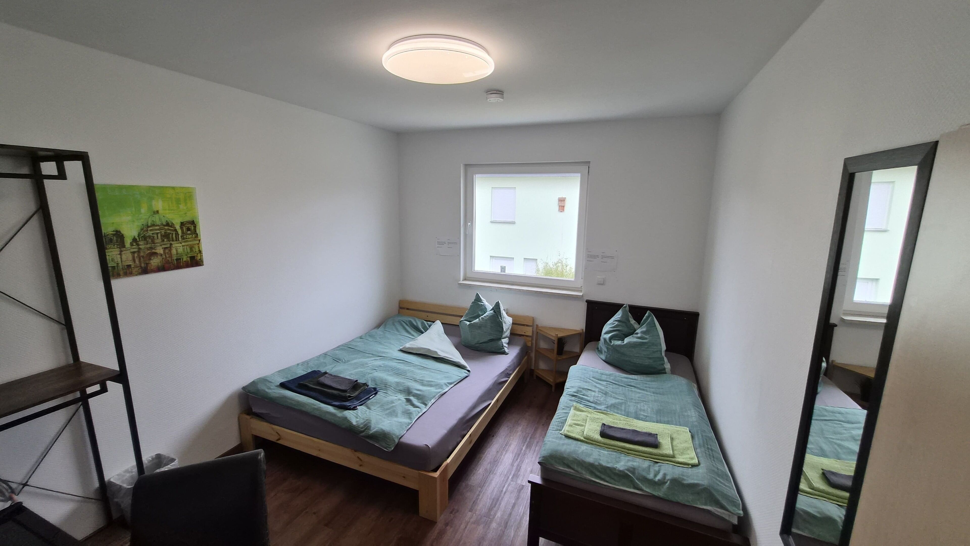 Un alojamiento pequeño y de una sola habitación, con dos camas, una ventana, piso de madera y una lámpara en el techo.
