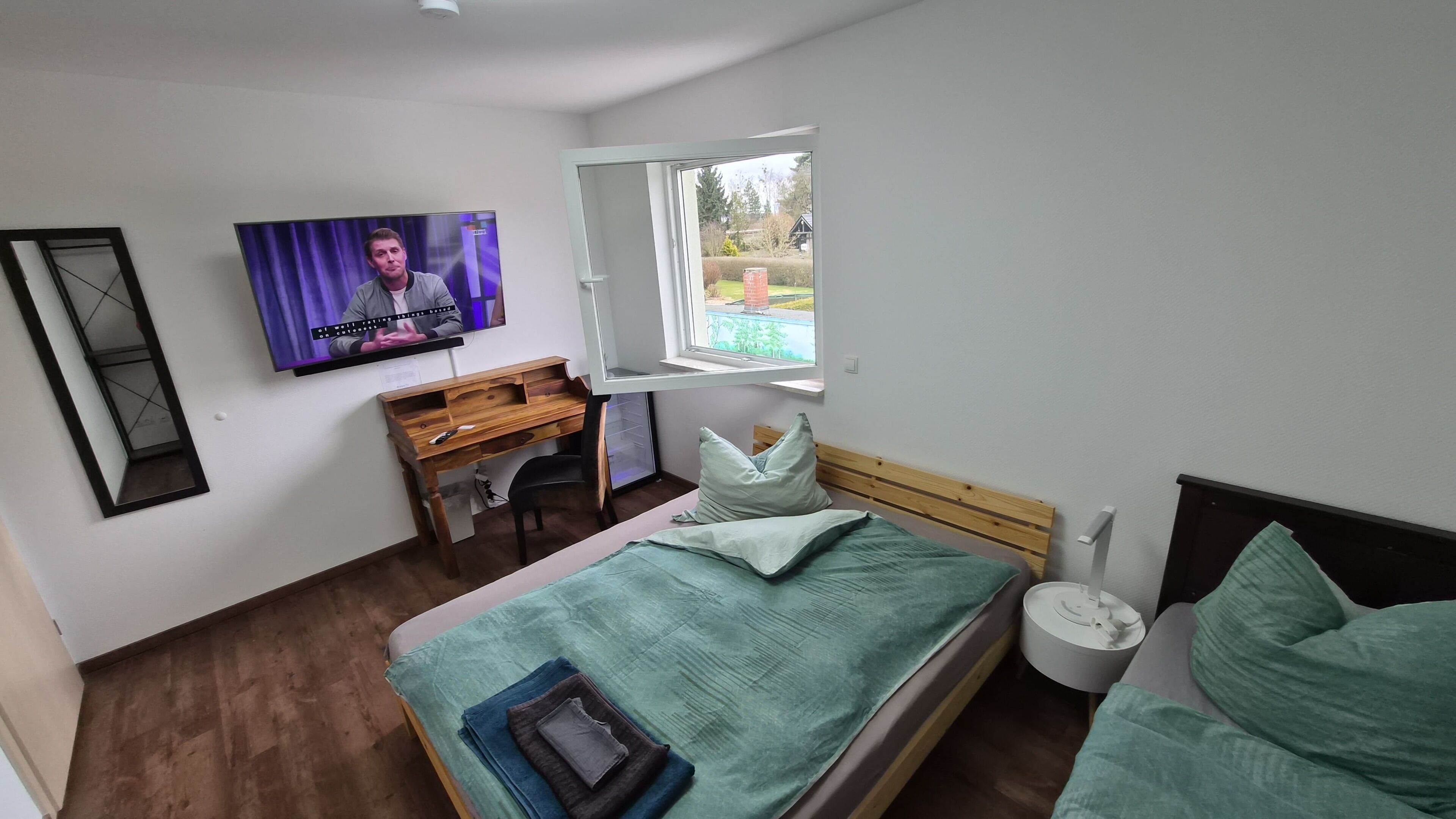 A bedroom with a bed, a desk, a chair, a television, and a window.