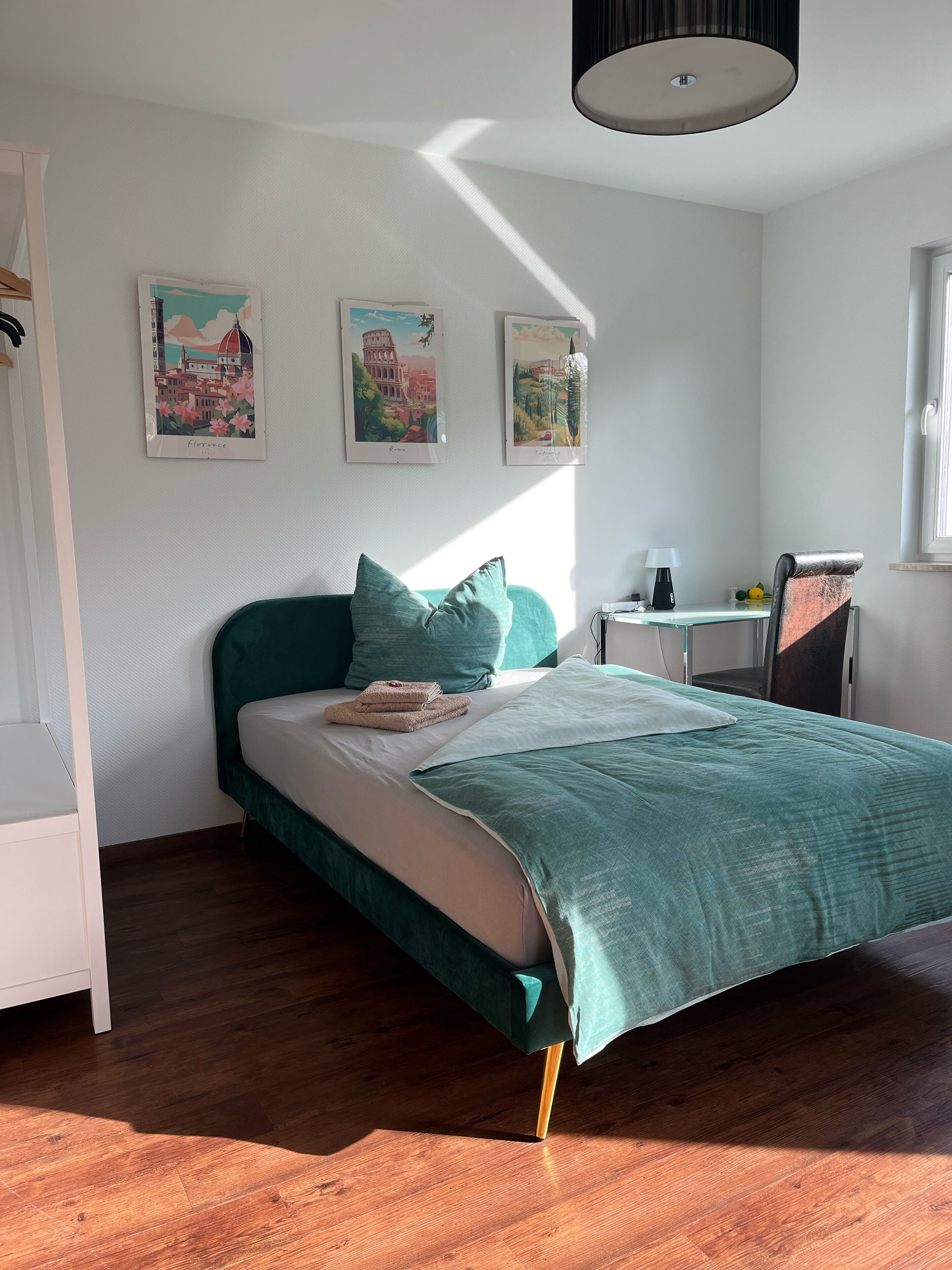 Ein Schlafzimmer mit einem Bett, einem Schreibtisch und einem Sessel. An der Wand hängen drei gerahmte Bilder.