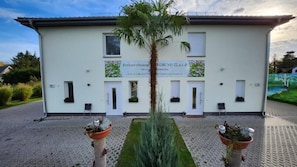 A building with a sign indicating it is a guesthouse. There are two potted plants in front of the entrance. - Ferienwohnungen im Grund 22 (Hoppegarten)